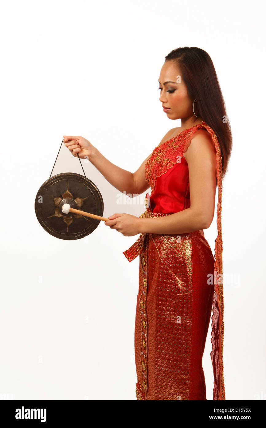 Belle jeune femme thaïlandaise dans une robe de satin rouge et or, la lecture d'un gong thaïlandais Banque D'Images