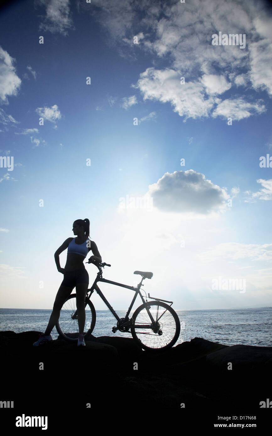 Hawaii, Oahu, Silhouette d'une femme avec un vélo sur une côte rocheuse. Banque D'Images