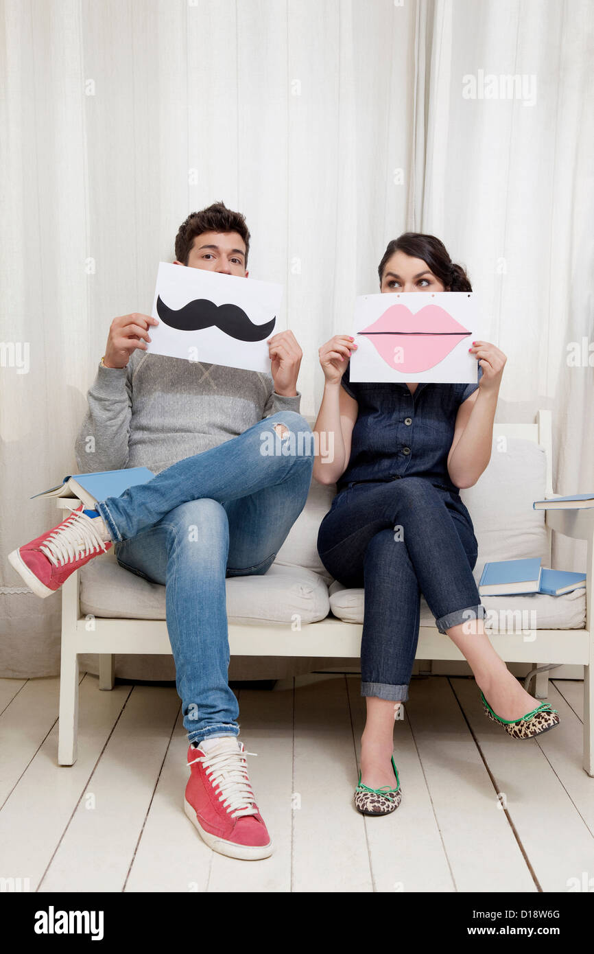 Couple sitting on sofa holding les lèvres et la moustache Banque D'Images