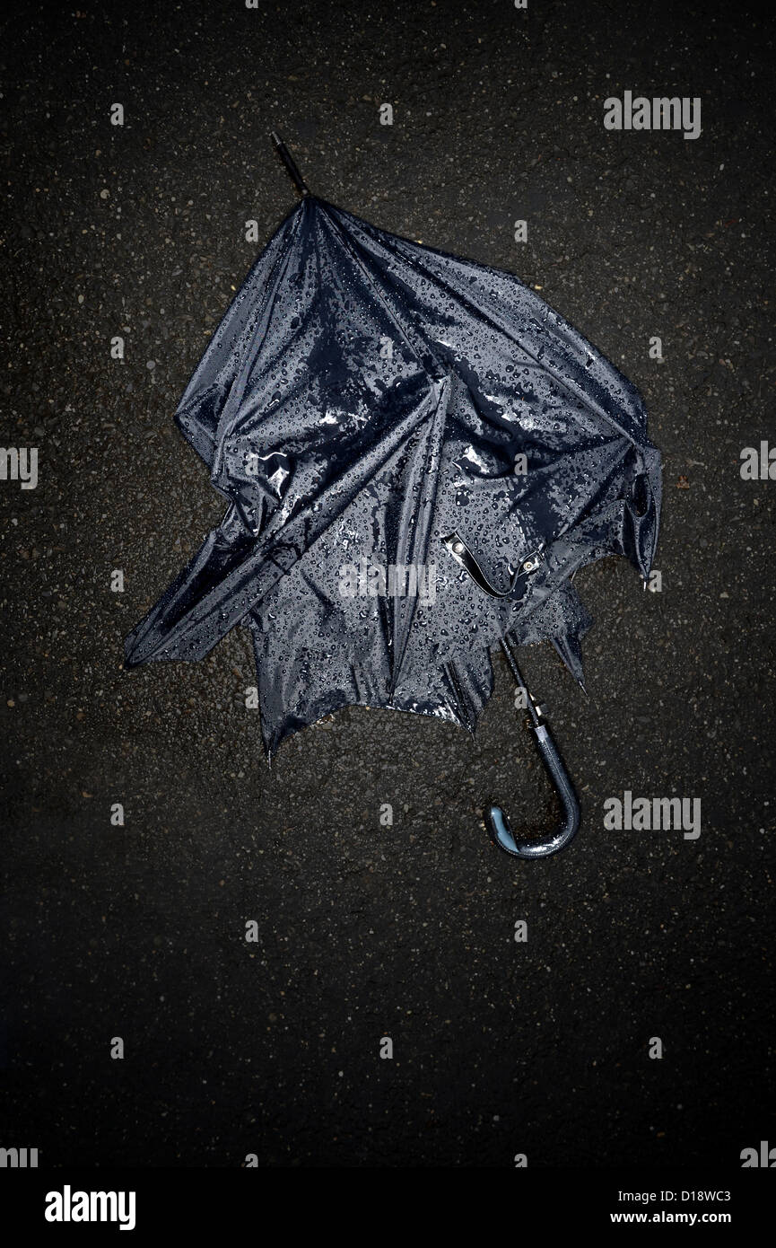 Parapluie noir cassé sous la pluie sur la rue noire Banque D'Images