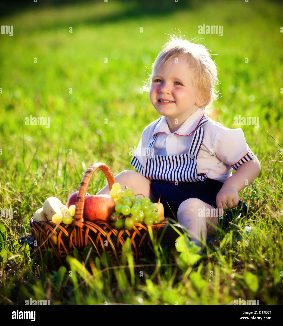 Petit garçon avec un panier de fruits est assis sur une herbe Banque D'Images
