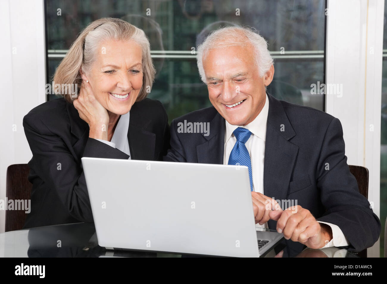Happy business couple looking at laptop sitting at table blanc Banque D'Images
