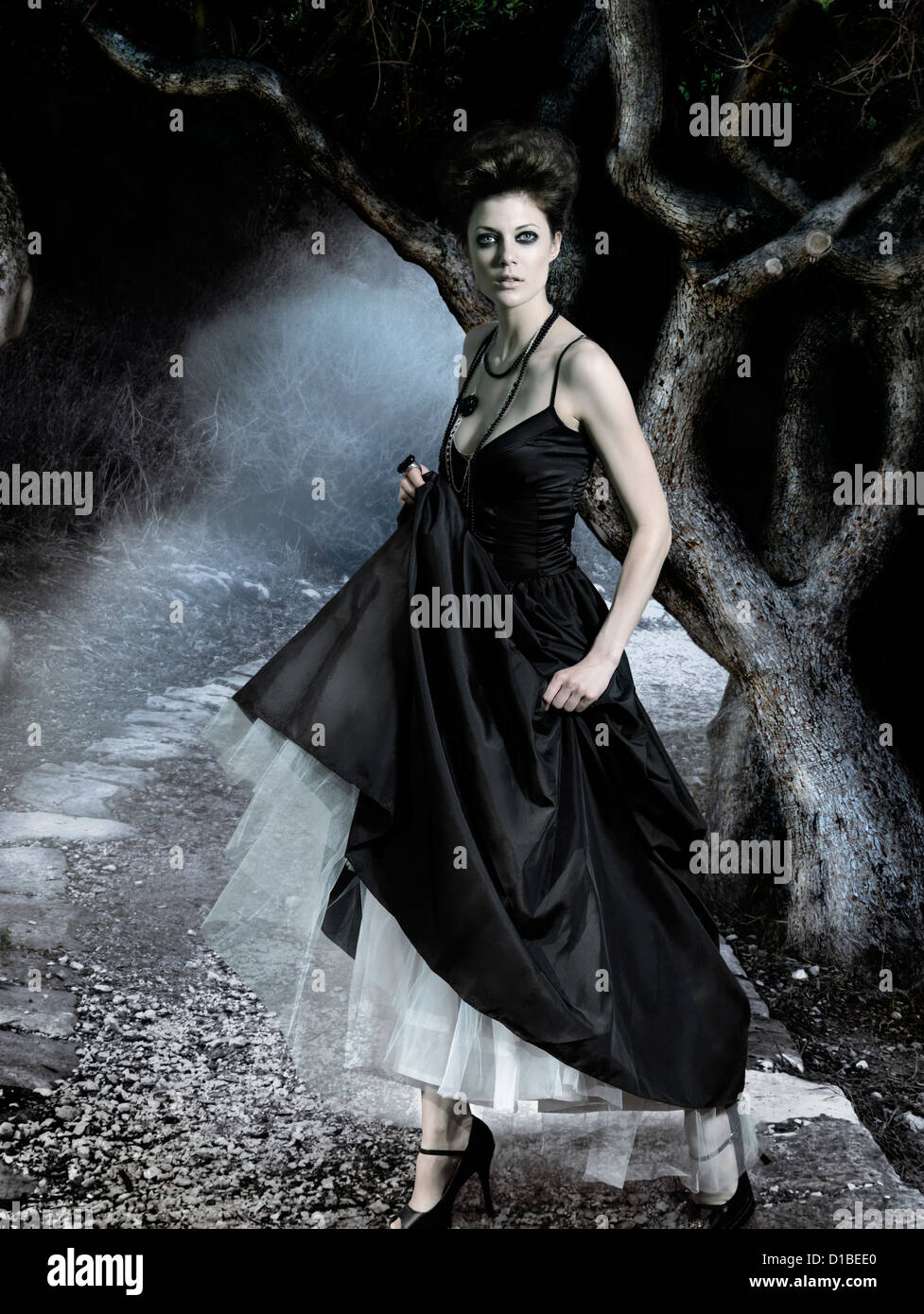 Belle jeune femme portant une robe noire classique dans une sombre forêt mystérieuse. Composé numériquement l'image. Banque D'Images