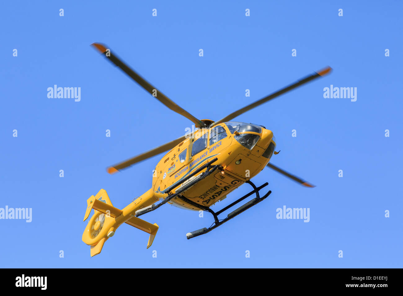Écossais jaune Air Ambulance Service hélicoptère volant au-dessus d'une mission de sauvetage vu du dessous contre un ciel bleu. UK Ecosse Sutherland Banque D'Images