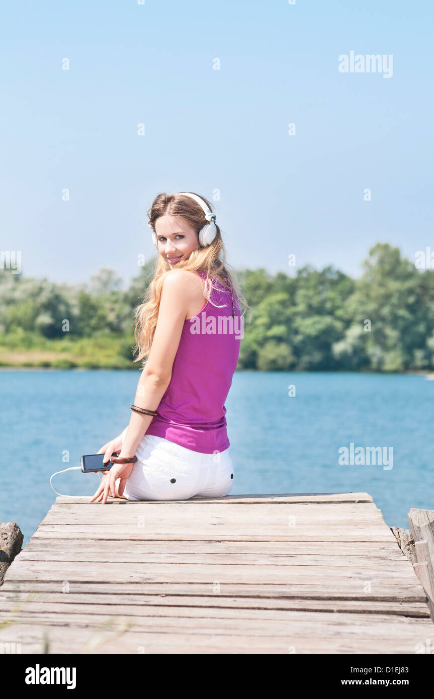 Jeune femme blonde avec un casque sur une jetée au bord d'un lac Banque D'Images