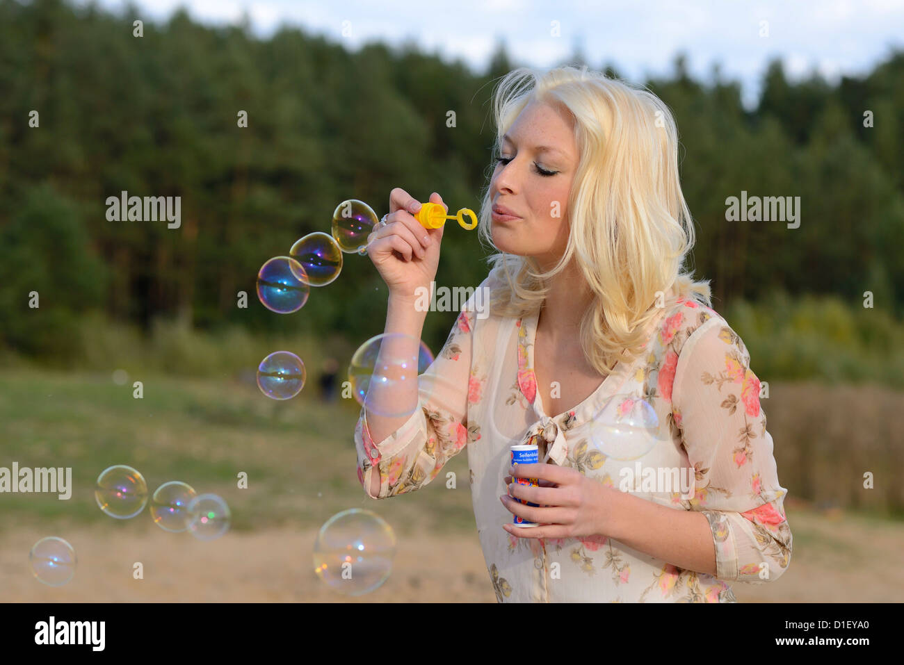 Happy young blonde woman blowing soap bubbles outdoors Banque D'Images