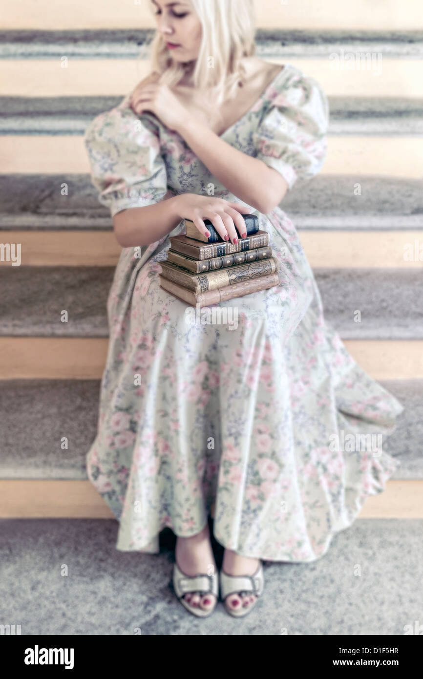 Une femme dans une robe florale tient une pile de livres anciens sur ses genoux Banque D'Images
