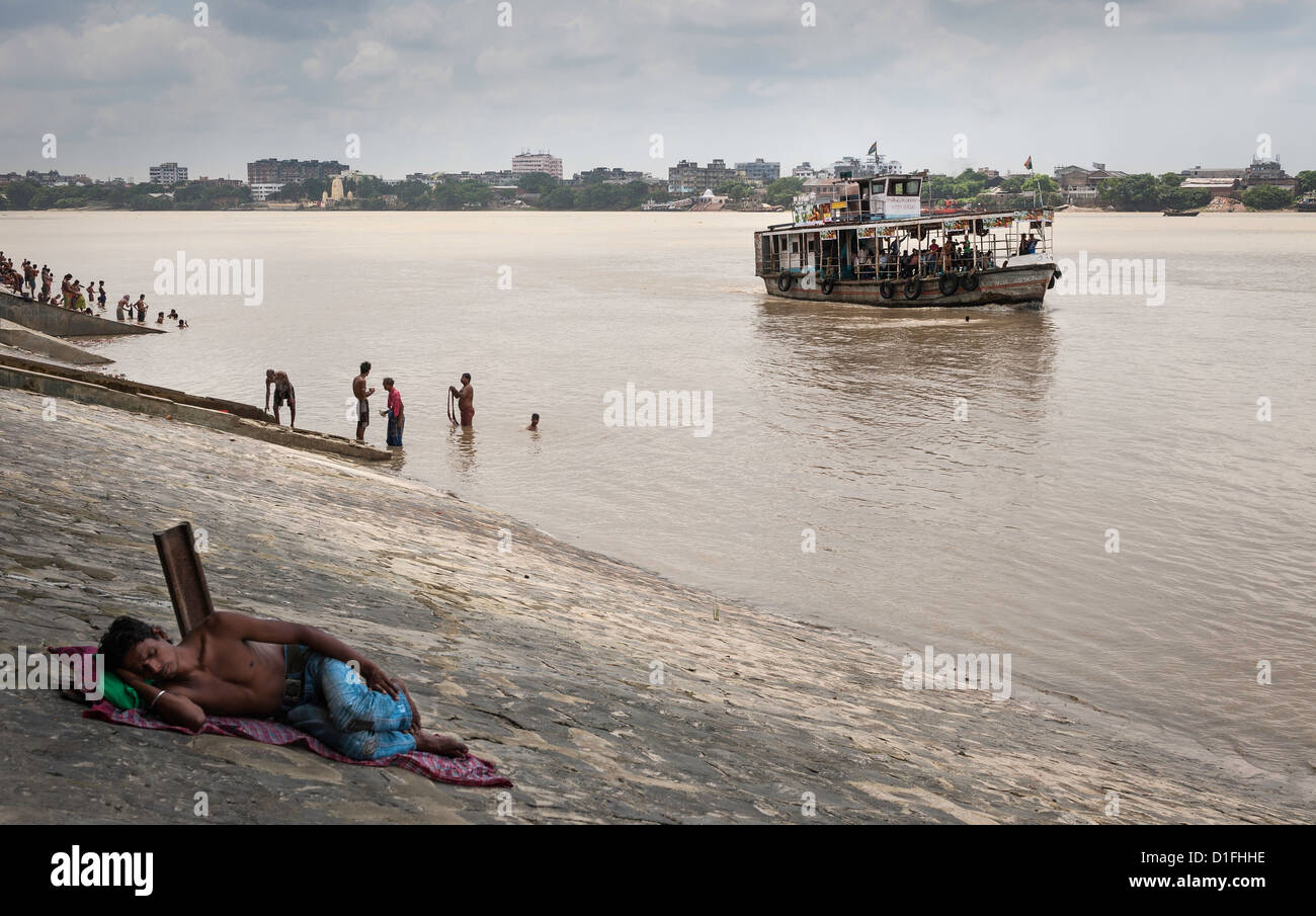 Bateau à passagers sur le Gange Howrah à Kolkata. Un homme est en train de dormir sur la rive du fleuve. Les baigneurs sont dans l'eau. Banque D'Images