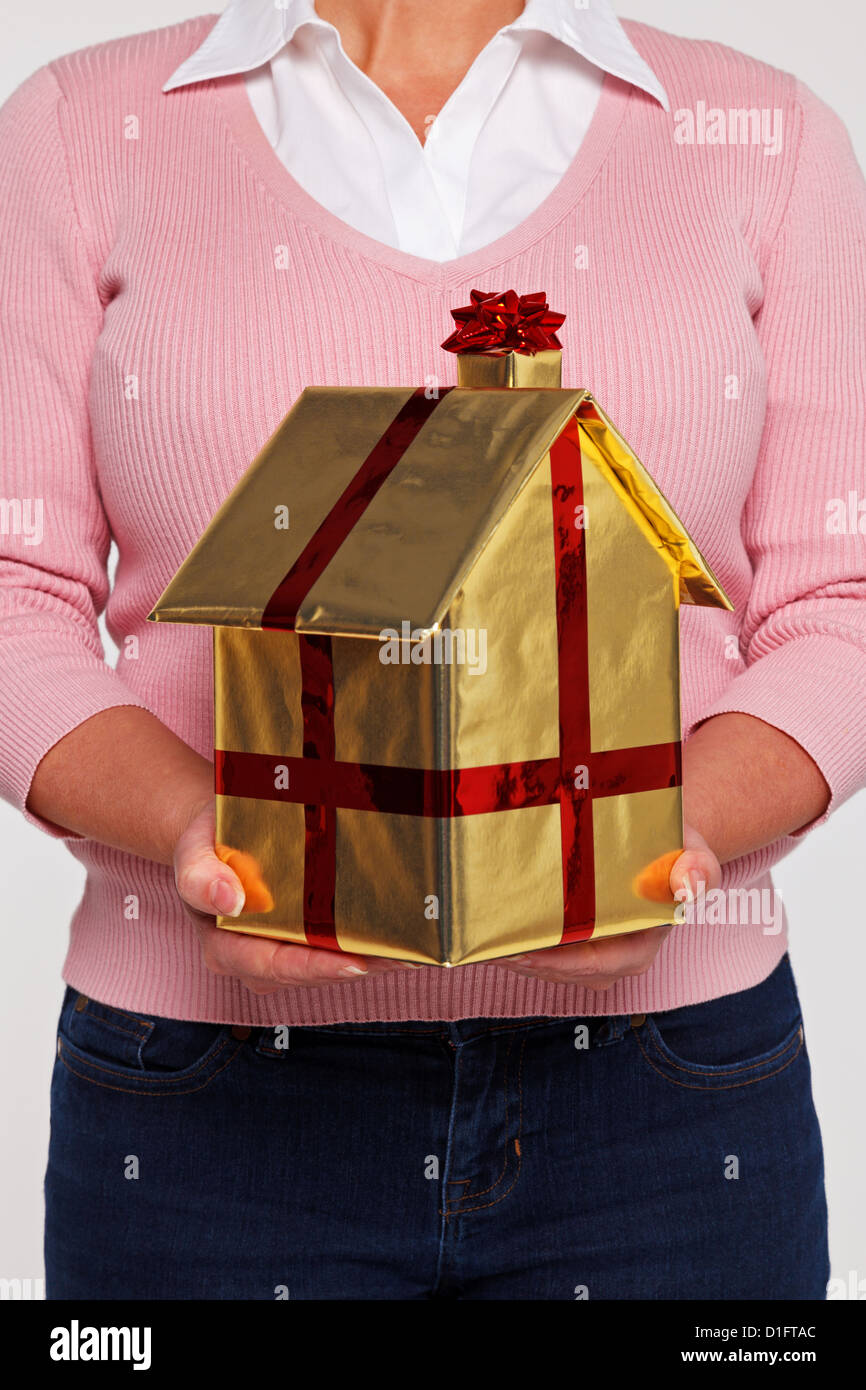 Nouvelles Accueil concept photo d'une femme en vêtements décontractés tenant un cadeau maison enveloppés dans du papier d'or avec ruban rouge et arc. Banque D'Images
