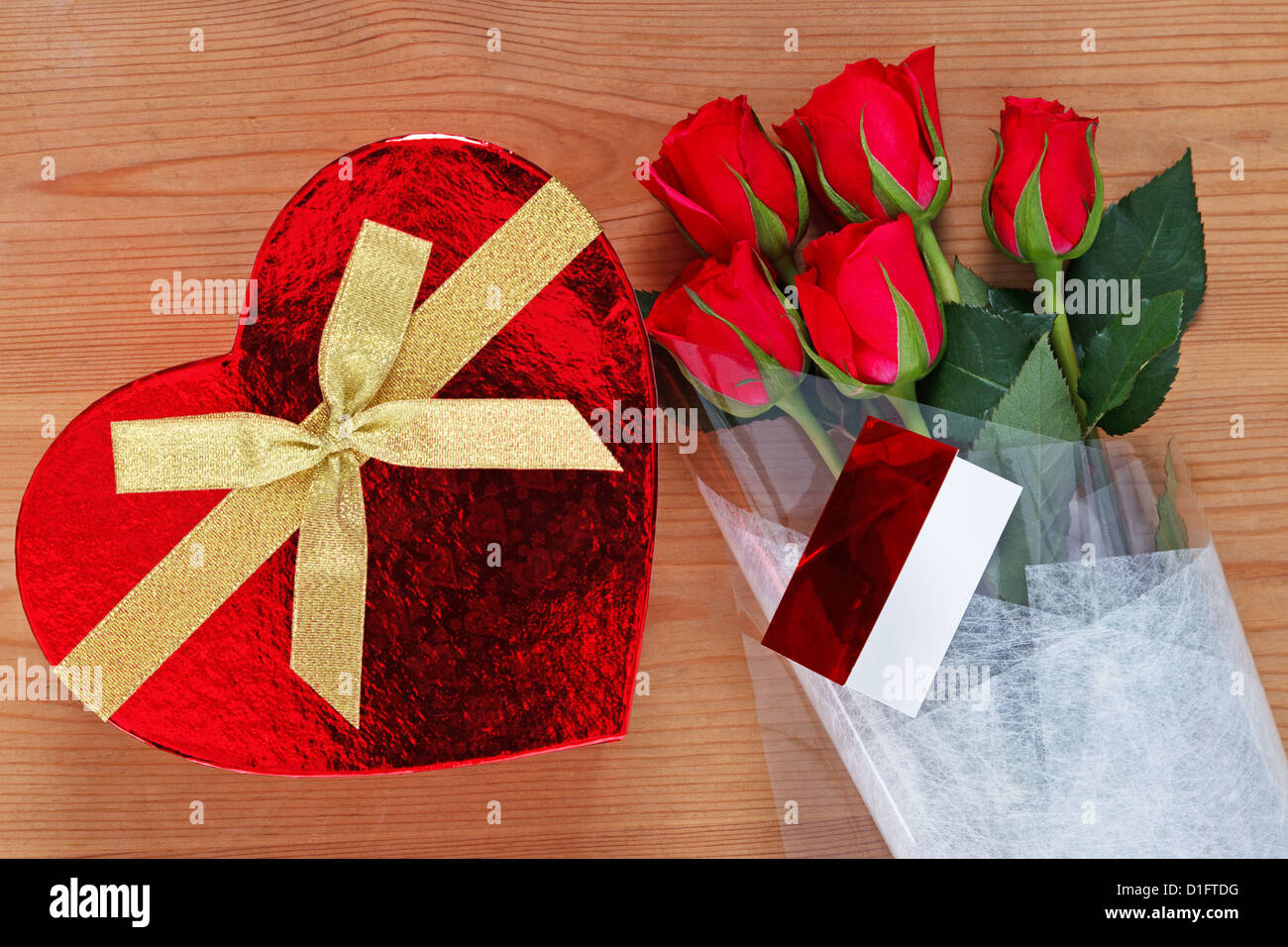 Des chocolats dans une boîte en forme de coeur et un bouquet de roses rouges avec la carte sur une vieille table en bois. Banque D'Images