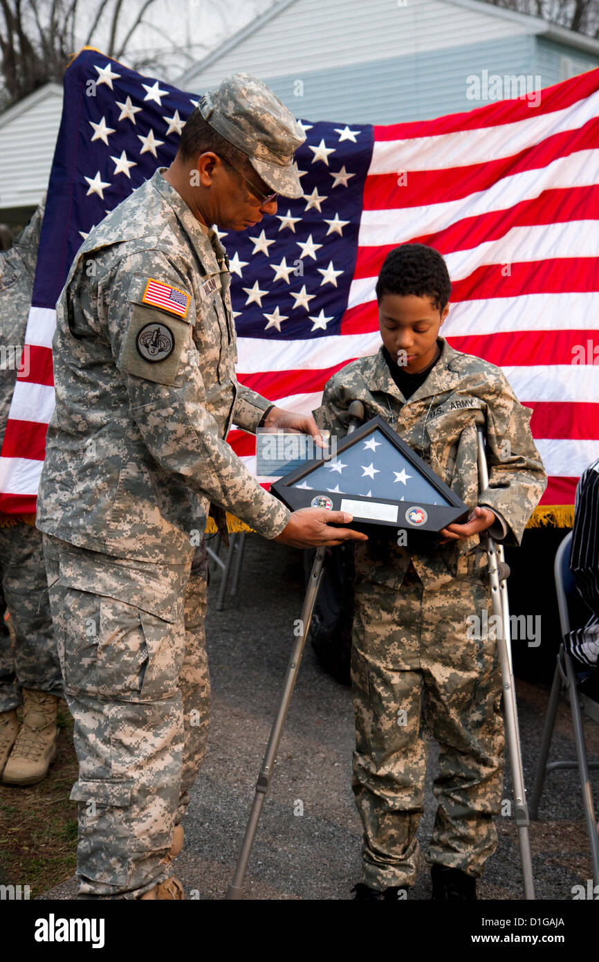 Le général Sanford Holman présente et drapeau américain à Khalil Quarles, 10, à la suite de son enrôlement à l'honneur à la réserve de l'armée le 20 décembre 2012 à Baltimore, MD. Khalil est le rêve d'être soldat mais souffre d'une forme rare de cancer terminal. Avec les soldats de la Police militaire du 200e Commandement a montré à la maison de Khalil et a tenu une cérémonie d'enrôlement et de fournir un uniforme, plaques, un drapeau, et un tour dans un Humvee blindés. Banque D'Images