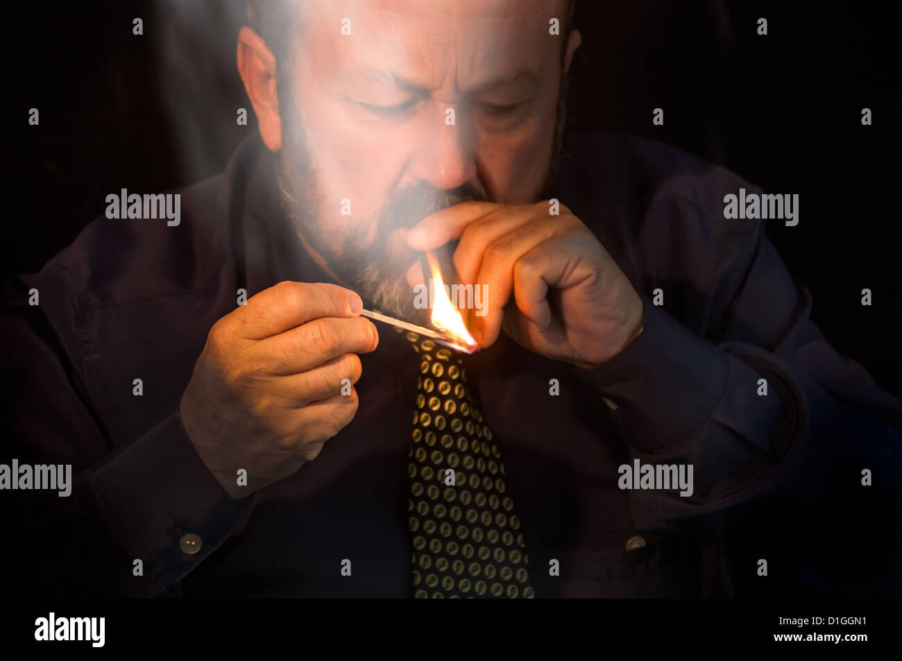 Homme d'allumer un cigare dans l'obscurité avec un long match Banque D'Images