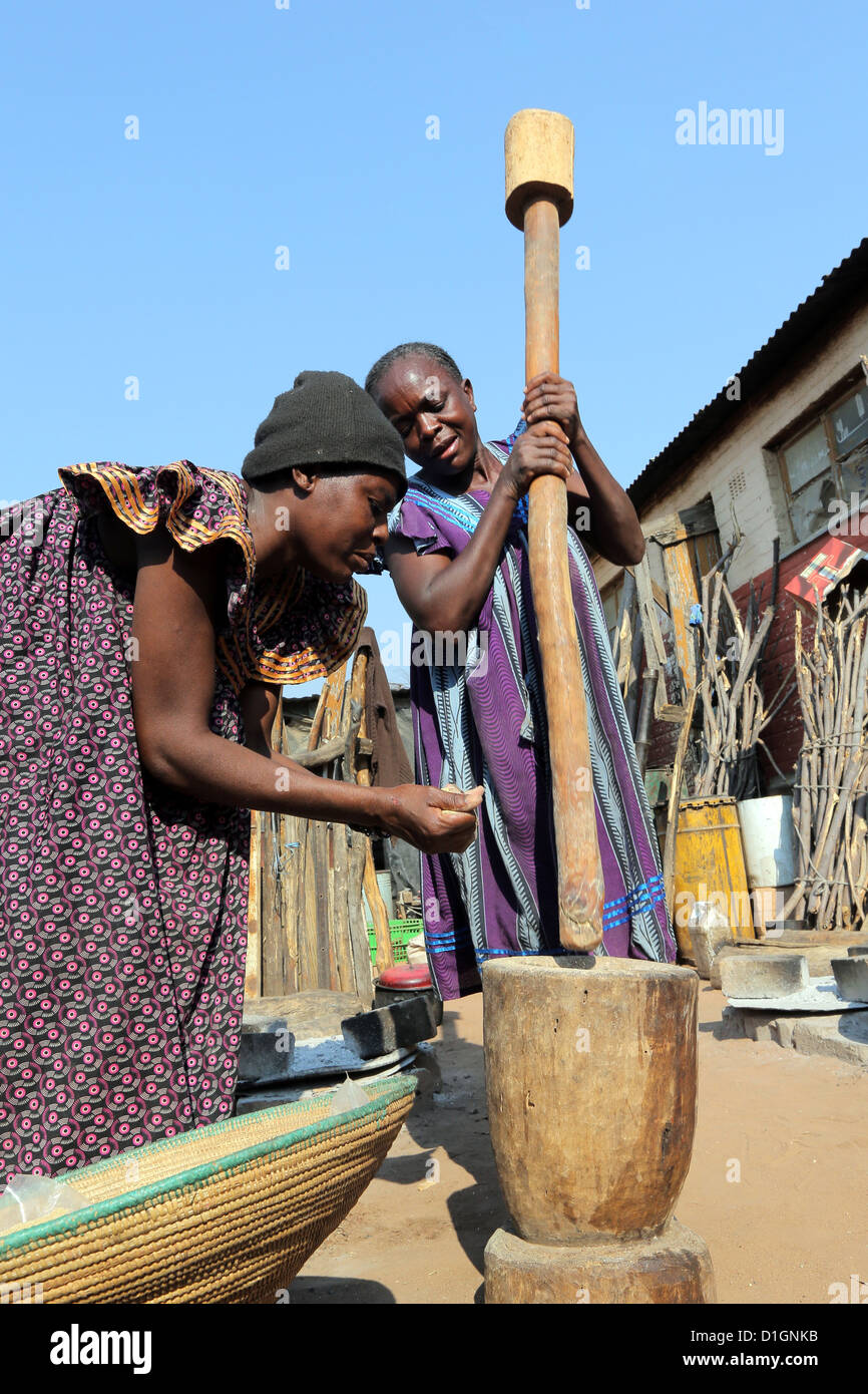 Deux femmes piler le mil (sorgum) à l'aide de mortier et pestel. Camp dans un pauvre alentours de Tsumeb, Namibie Banque D'Images