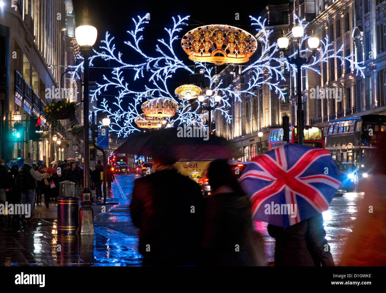Londres Noël pluie nuit reflets shoppers mouillés, parapluie drapeau Union Jack dans Regent Street mouillé pluvieux avec des lumières de Noël derrière la nuit Londres Royaume-Uni Banque D'Images