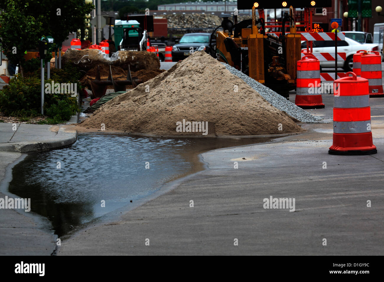 Tas de sable retient une petite flaque d'eau sur un site de construction de la rue. Banque D'Images