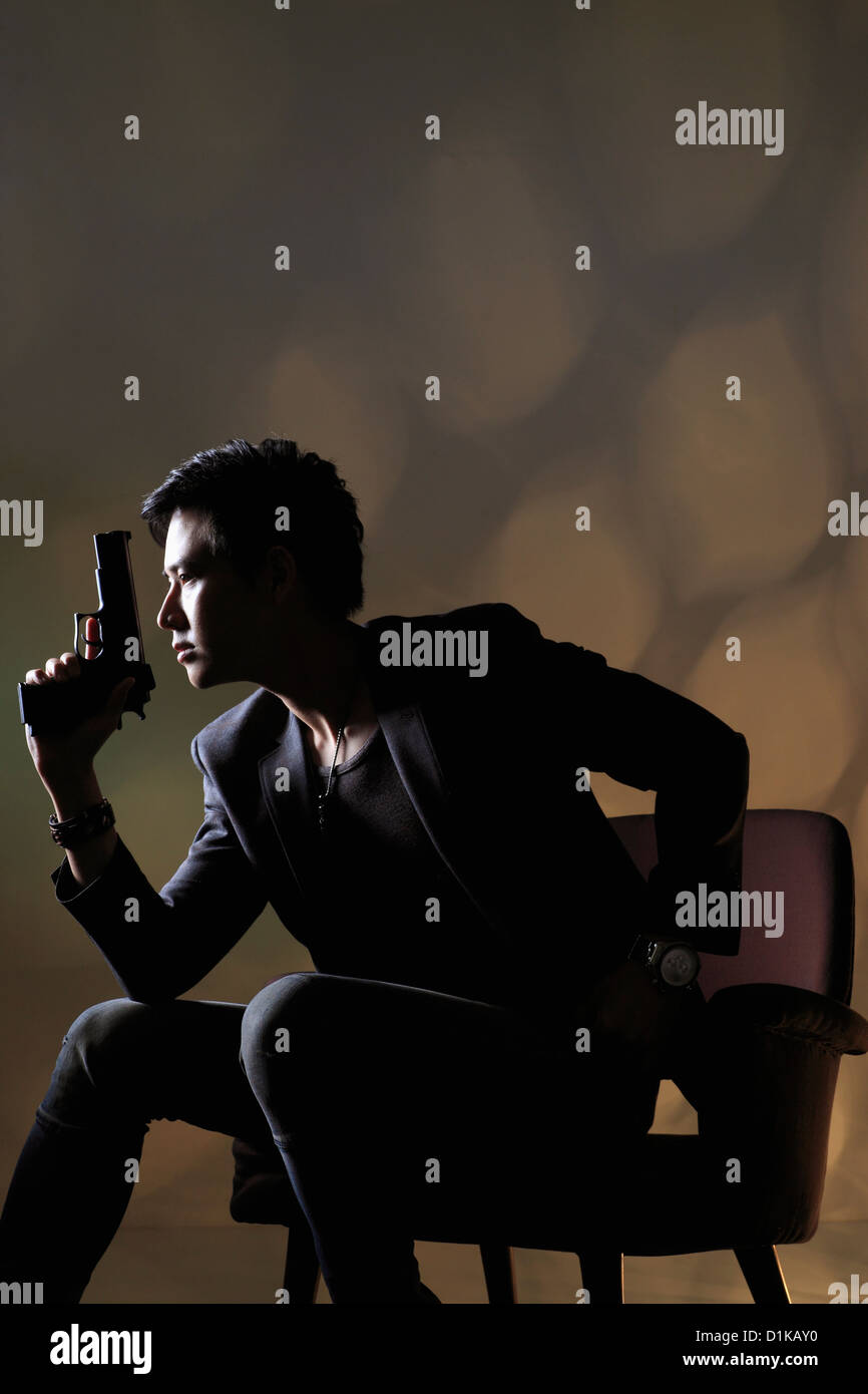 Profil de jeune homme assis tenant un pistolet. Banque D'Images