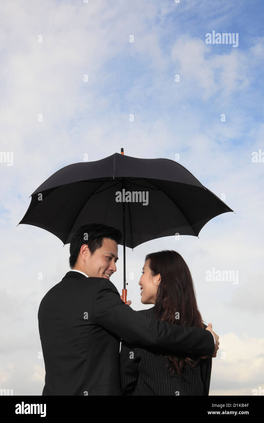 Vue arrière du couple tenant un parapluie noir souriant à l'autre. Banque D'Images
