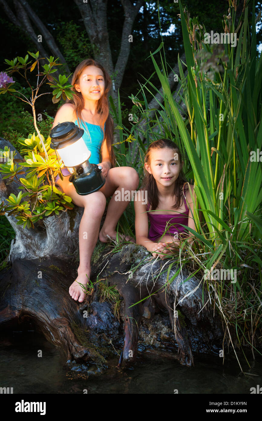 Mixed Race sisters sitting on riverbank avec lanterne Banque D'Images