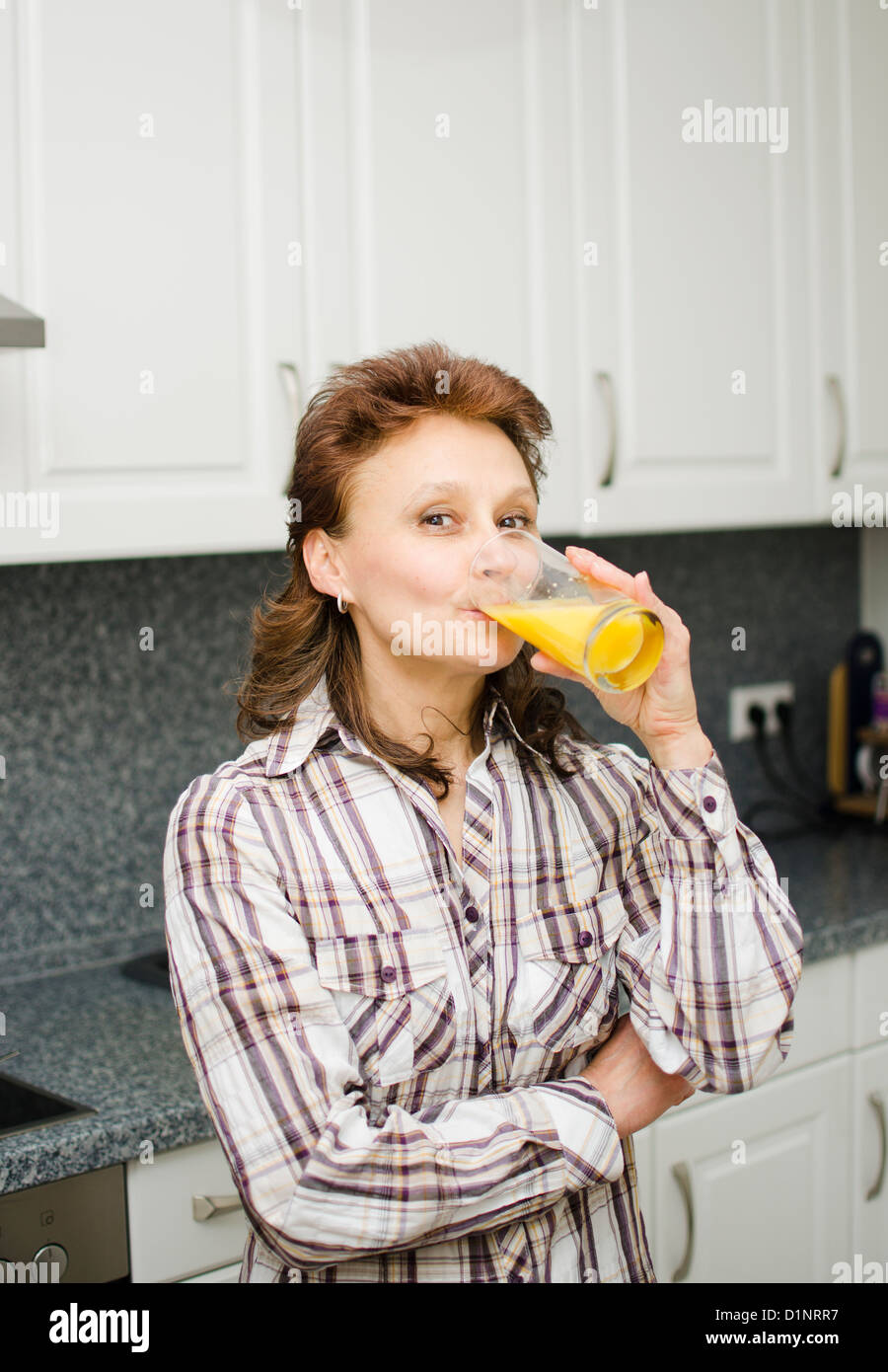 Une femme avec un verre de jus d'orange dans la cuisine. Banque D'Images