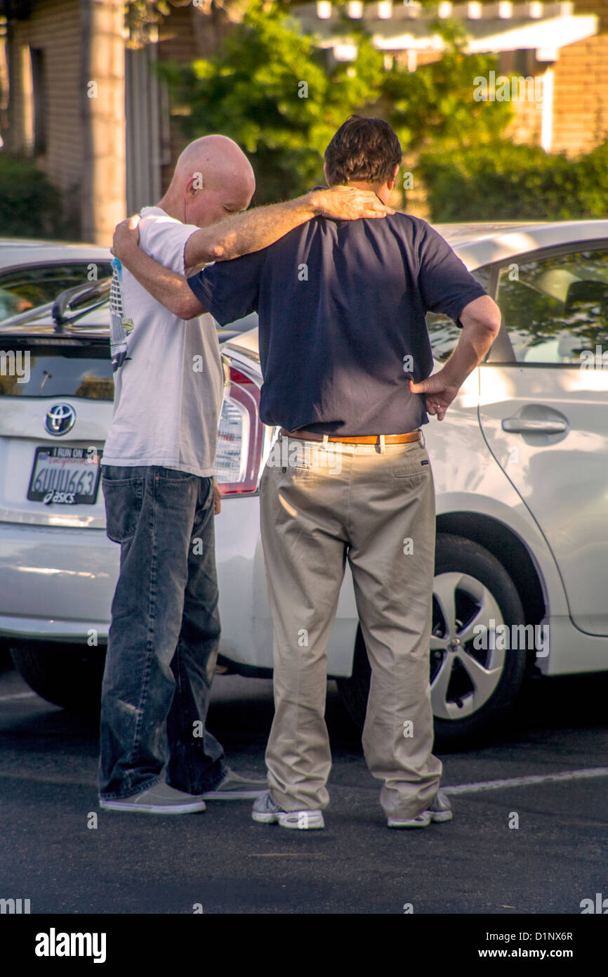Bras dessus bras dessous, deux hommes prier ensemble dans une Laguna Niguel, CA, un parking. Banque D'Images