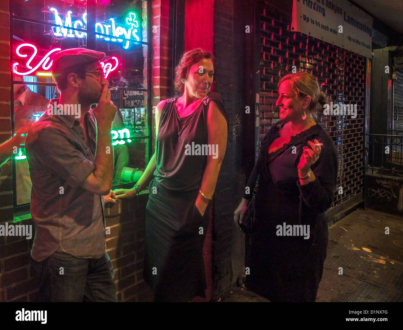 Un homme et deux femmes fument sur le trottoir à l'extérieur d'un restaurant de nuit sur New York City's Lower East Side. Banque D'Images