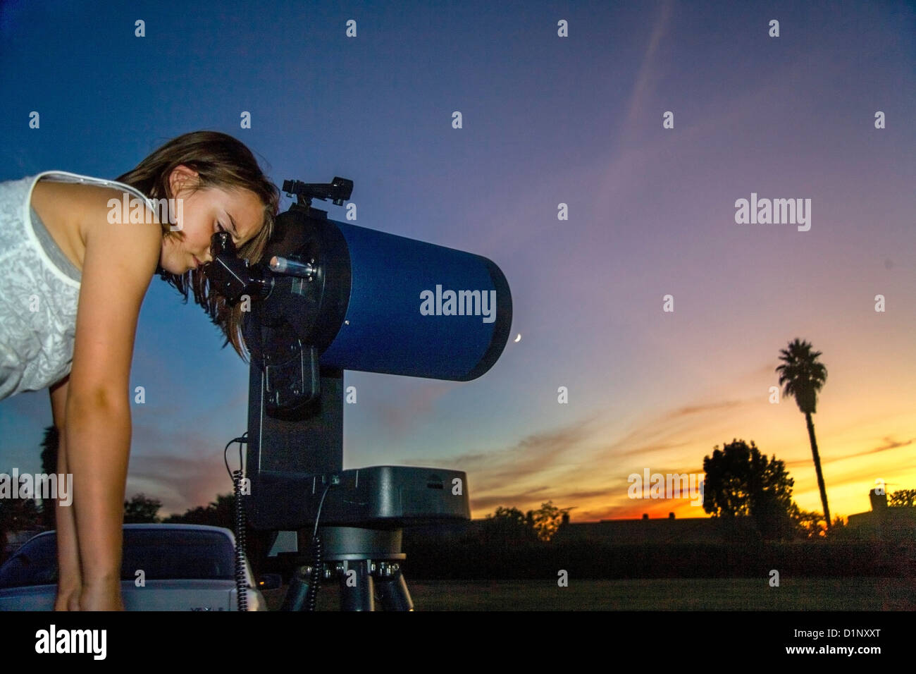 Au crépuscule, une fillette de huit ans a l'air à travers l'oculaire d'un télescope catadioptrique dans son arrière-cour de la Californie. Banque D'Images