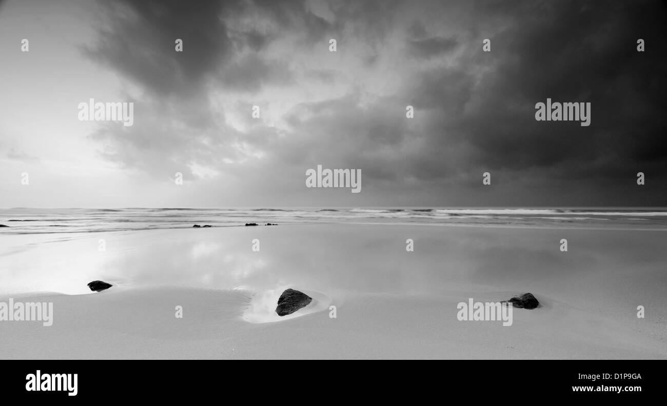 Noir et blanc paisible paysage de plage avec trois pierres sous un ciel d'orage bleu Banque D'Images