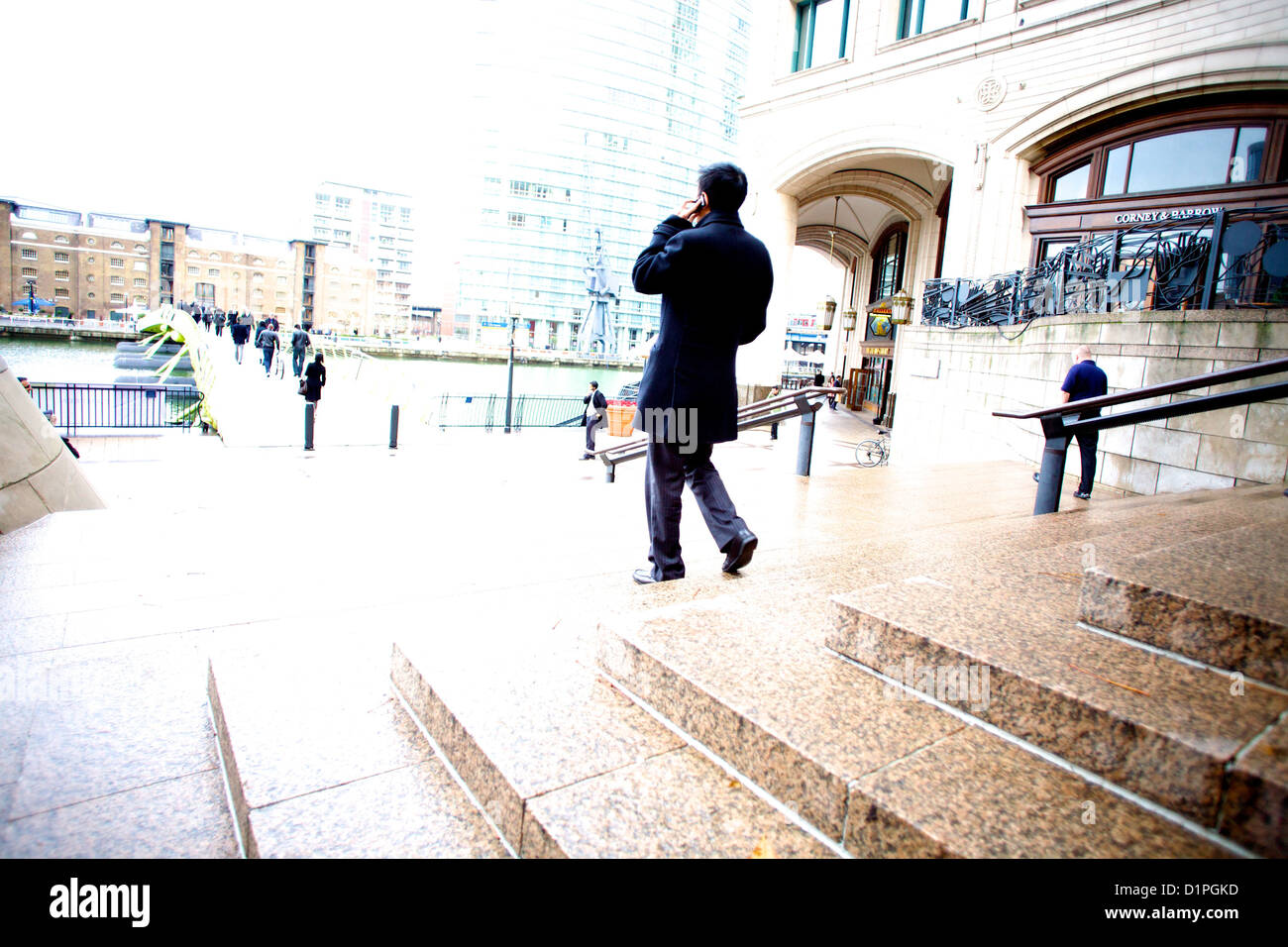 Man in black coat talking on mobile phone while walking down steps dans le quartier des affaires de Canary Wharf, Banque D'Images