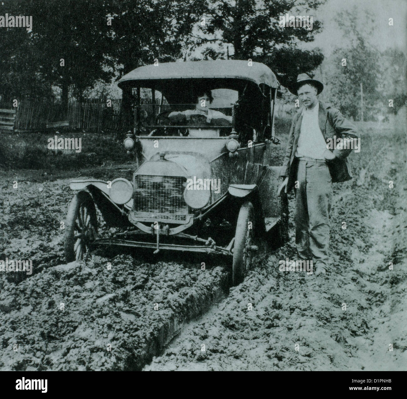Femme en voiture Ford modèle T sur route boueuse avec l'Homme debout à côté d'elle, début des années 1900 Banque D'Images