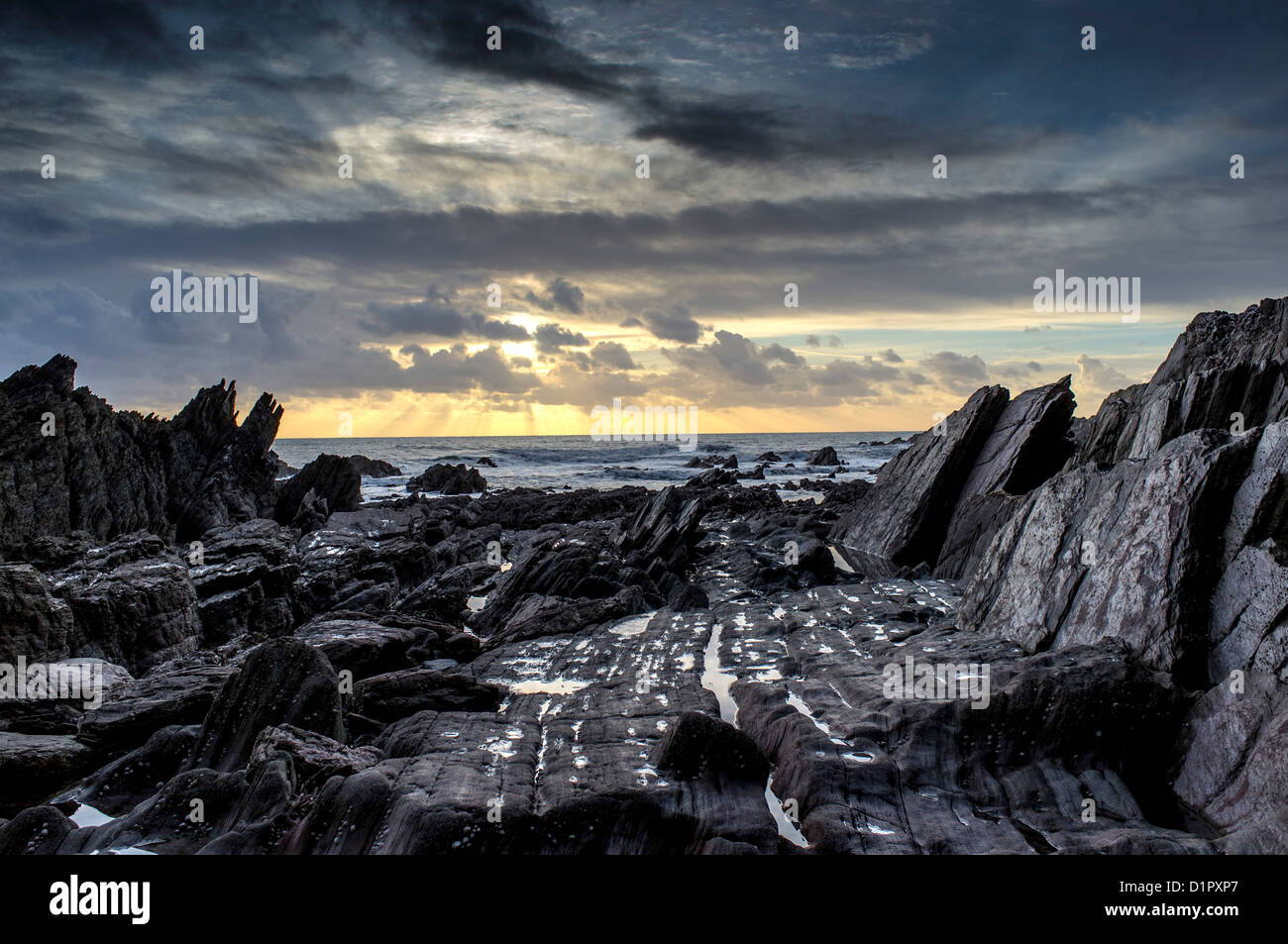 Vue spectaculaire sur un soleil d'hiver au-dessus de la mer depuis une plage de formations rocheuses inhabituelles et humides. Ayrmer Cove, Devon. ROYAUME-UNI Banque D'Images