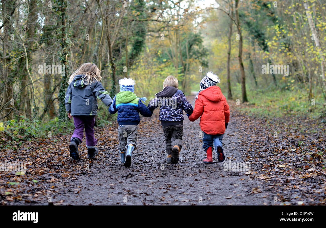 Quatre enfants se tenant la main marchant dans un chemin boisé s'amusant Banque D'Images