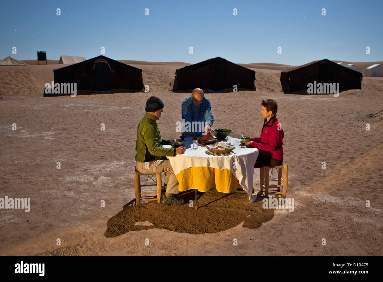 Le Maroc, M'Hamid, Erg Chigaga dunes de sable. Désert du Sahara. Camp de vacances, un bivouac. Les touristes en train de dîner à la pleine lune la lumière. Banque D'Images