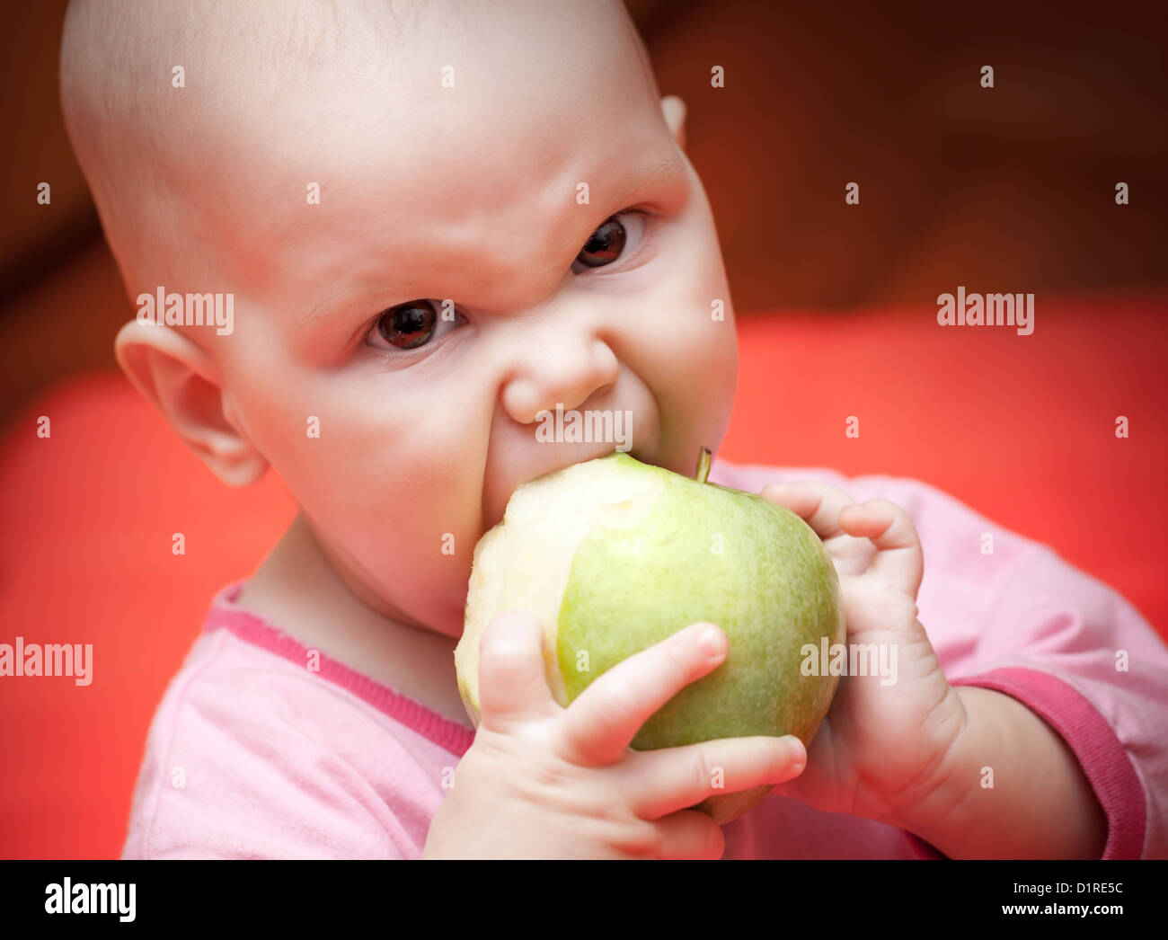 Drôle de petit bébé affamé dans un dossier rose vert pomme juteuse mange avidement Banque D'Images