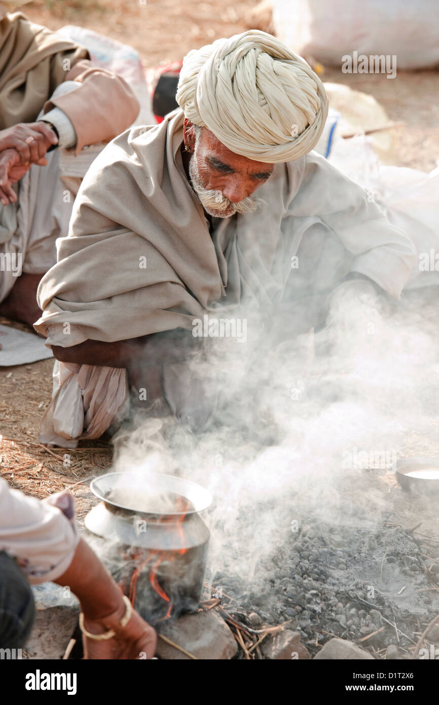 Négociant un chameau dans un turban blanc prépare une parmi la fumée d'un feu de camp dans le désert à l'extérieur de Pushkar Rajasthan Inde Banque D'Images