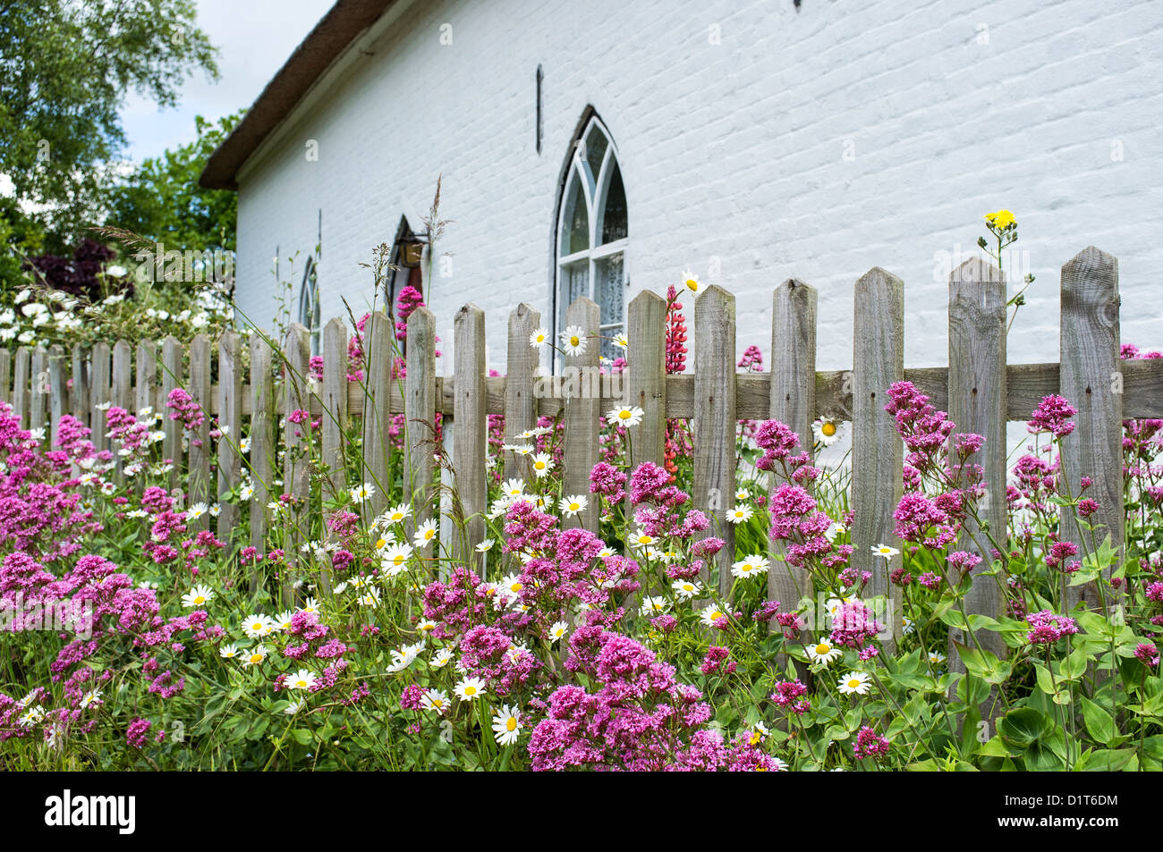 Chalet peint en blanc avec des fleurs sauvages de croître autour de Picket Fence Banque D'Images