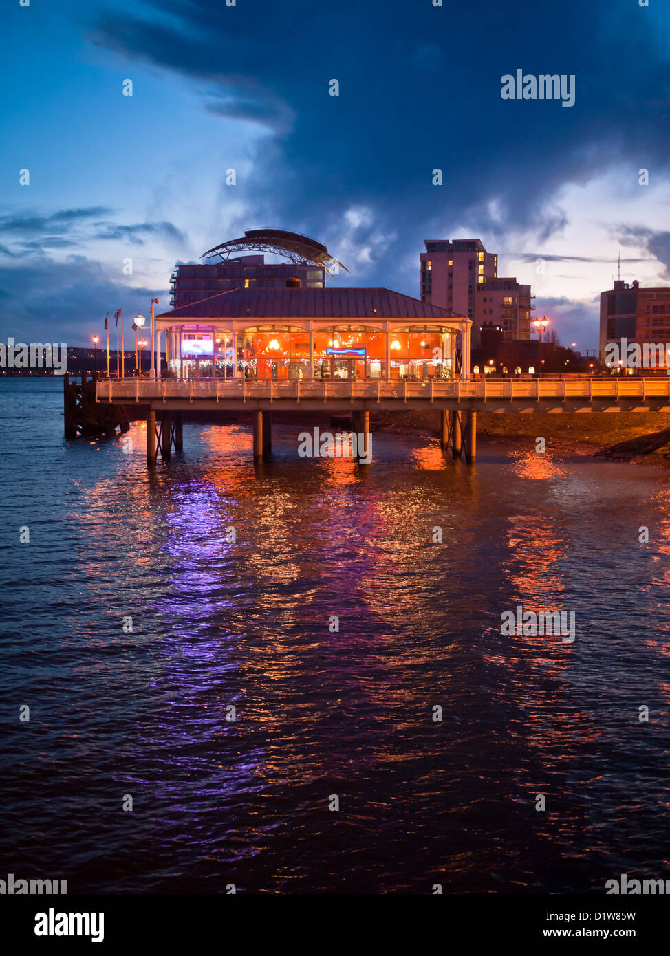 Les nuages sombres de Mermaid Quay, passez au-dessus de la baie de Cardiff, Pays de Galles, au crépuscule. Les lumières colorées de l'embarcadère de tenir compte de la surface de la mer. Banque D'Images