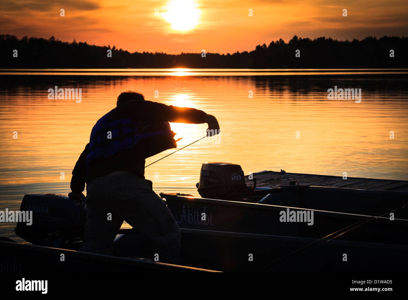 Silhouette de pêcheurs qui démarre le moteur de son bateau avec le jaune et l'orange soleil dans l'arrière-plan Banque D'Images