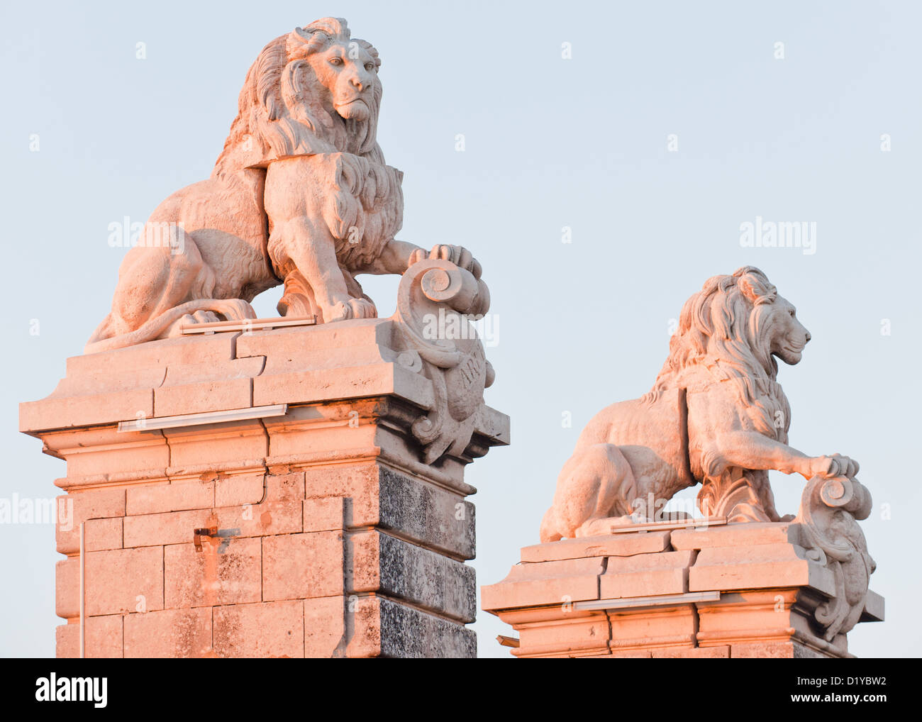 Deux majestueux Lion en pierre sculptures dans la ville d'Arles, France. Un côté est bien éclairée par le coucher du soleil orange. Banque D'Images