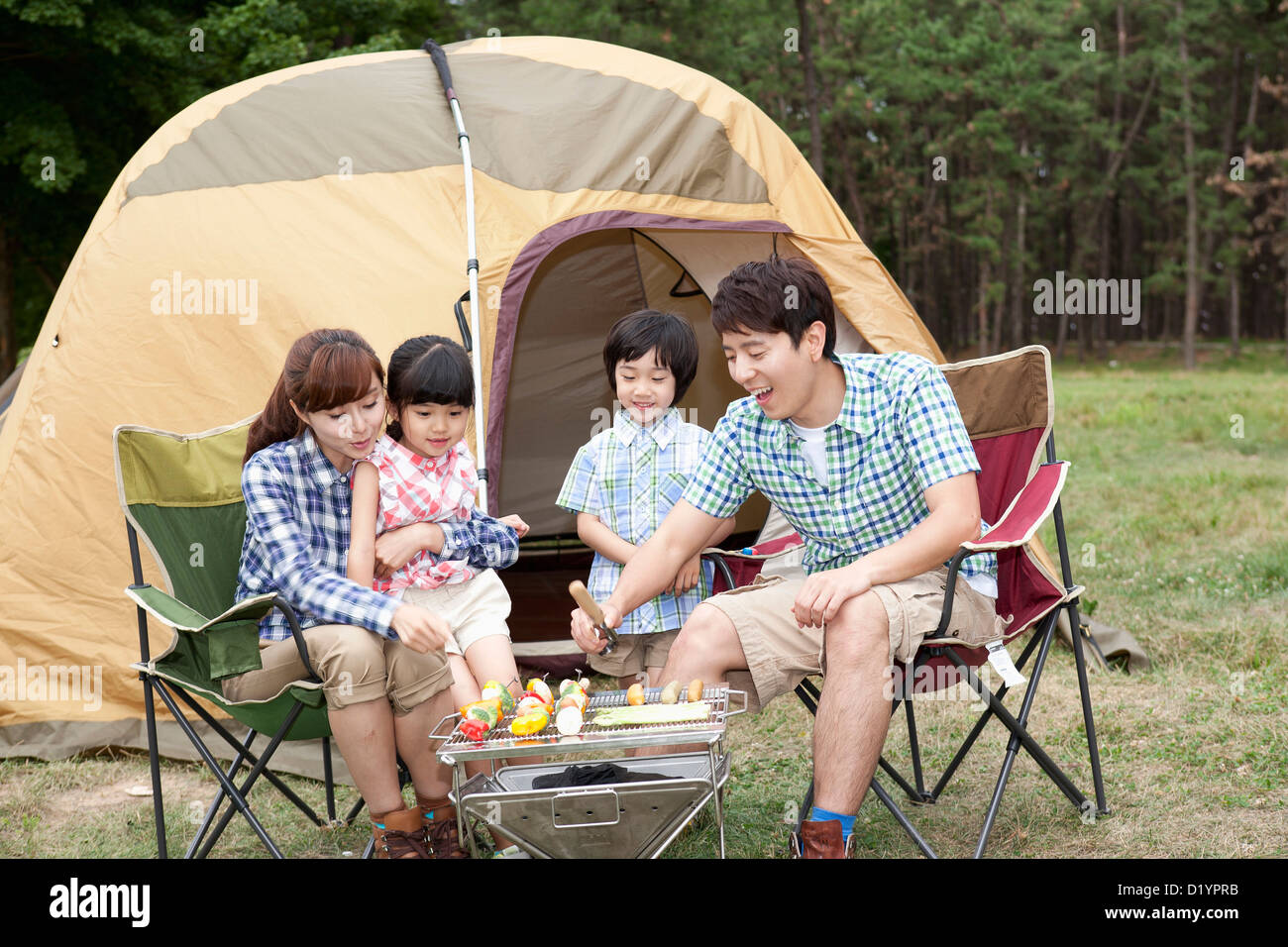 Famille assis sur chaises de camping grilling food Banque D'Images