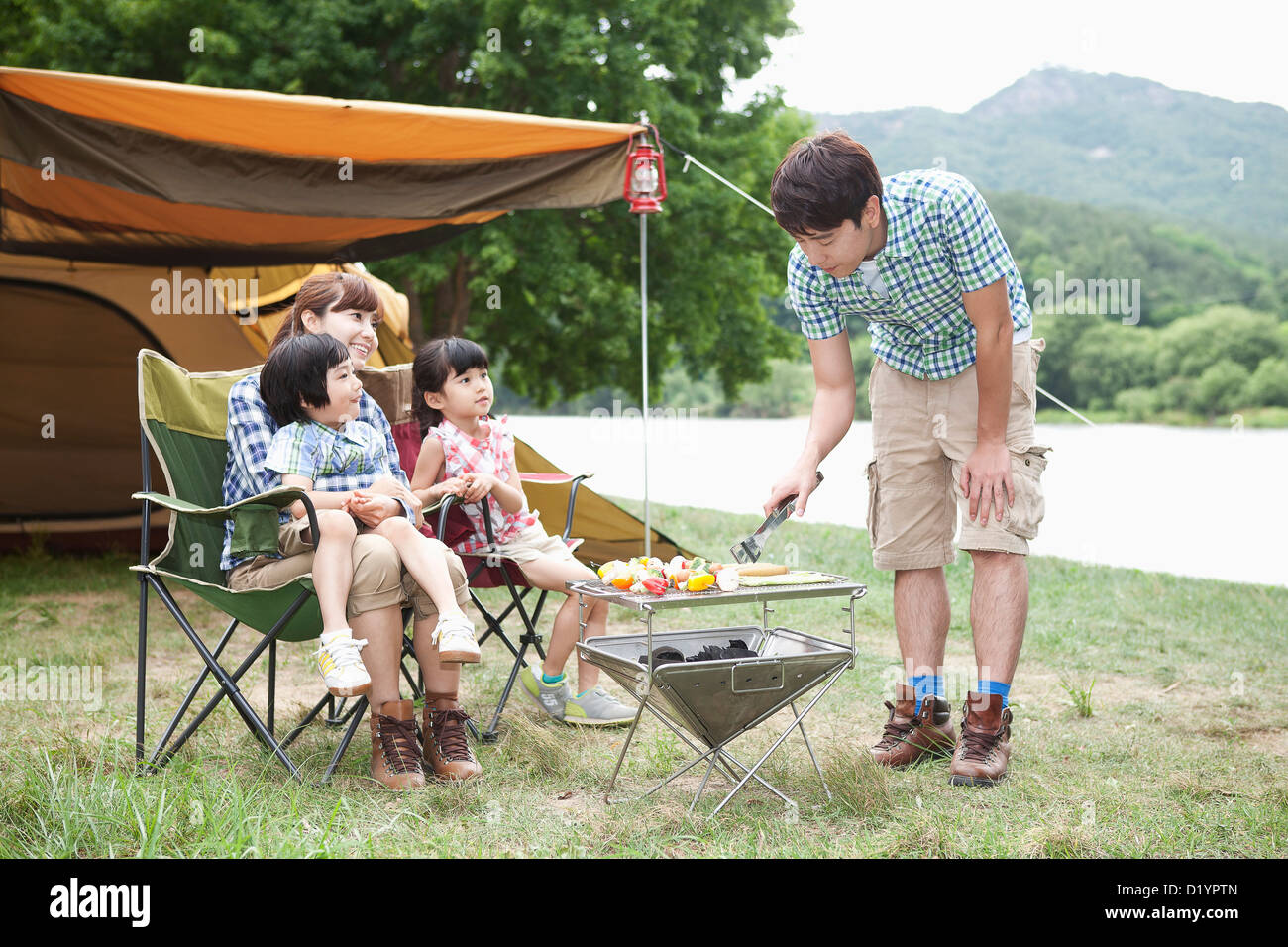 Cuisson tandis que le père d'autres membres de la famille assis sur chaises de camping Banque D'Images