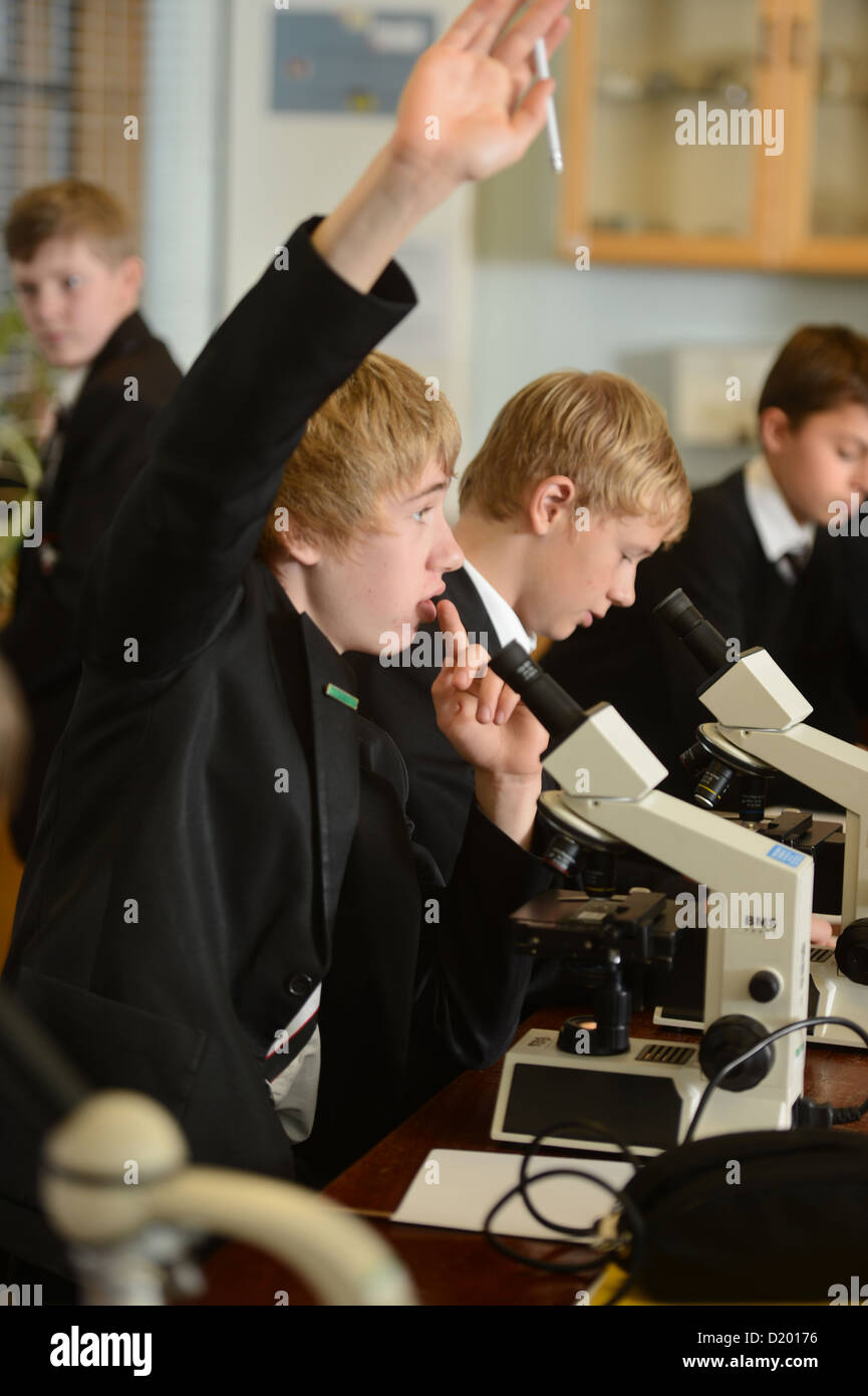 Un garçon de l'école pose une question tout en utilisant un microscope pendant une leçon de science à Pates Grammar School à Cheltenham, Gloucesters Banque D'Images