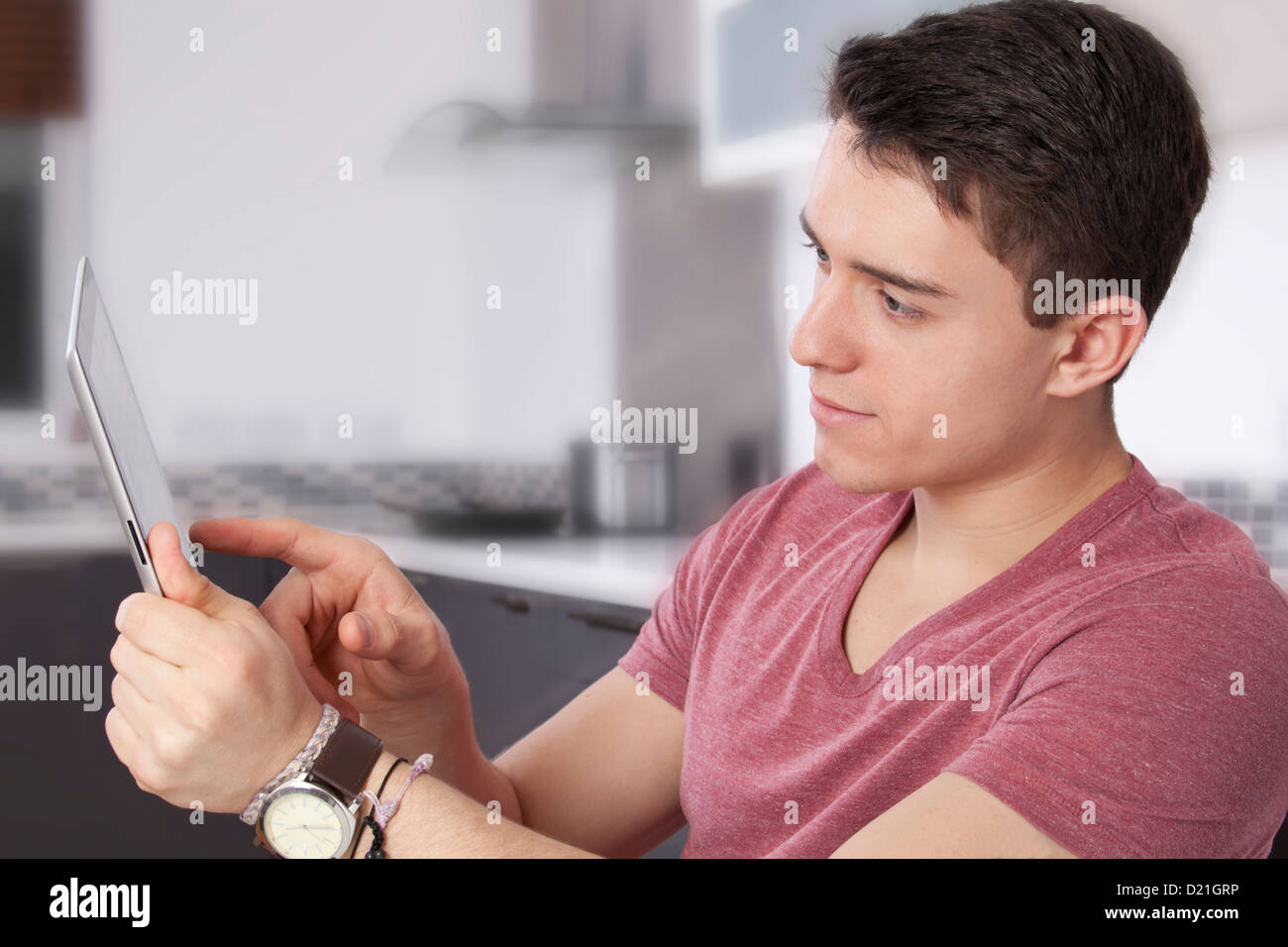 Jeune homme à l'aide d'une tablette numérique, regarder l'écran ou moniteur. Situé dans une cuisine moderne. Banque D'Images