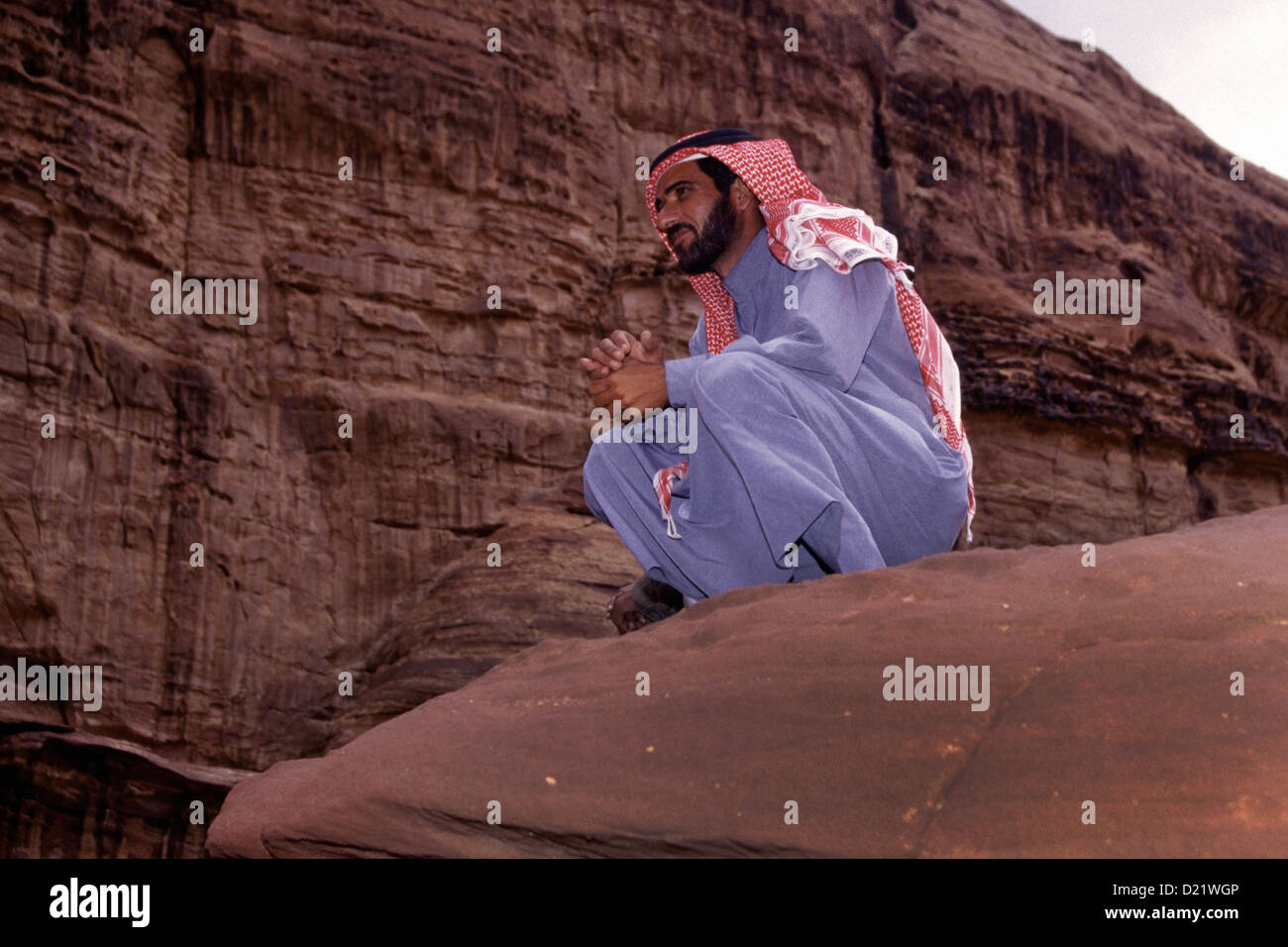 Un homme assis sur une falaise portant keffieh ou kufiyain aussi connu comme ghutrah coiffure traditionnels arabes dans le désert de Wadi Rum Canyon Khazali connu aussi sous le nom de la vallée de la lune, dans le sud de la Jordanie Banque D'Images