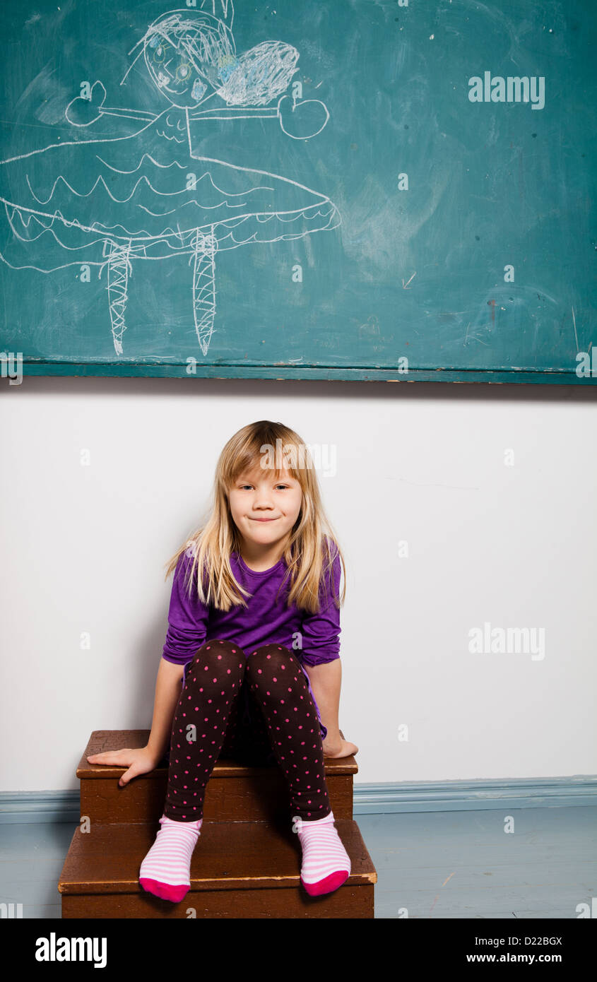 Studio portrait of smiling young girl sitting in classroom en face du tableau sur le dessin Banque D'Images