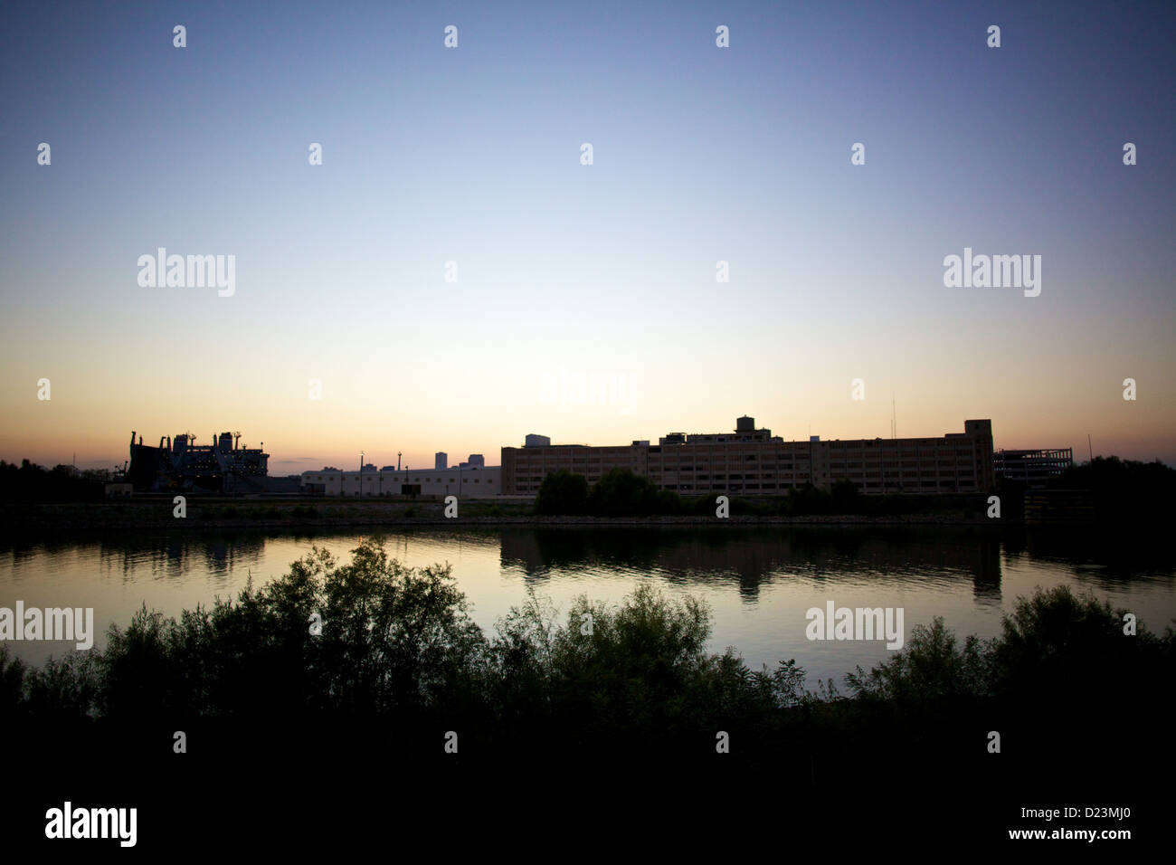 Coucher de soleil en Louisiane sur Baton Rouge avec des silhouettes de bâtiments industriels reflétés dans des eaux calmes, avec des teintes bleues, roses et oranges douces Banque D'Images