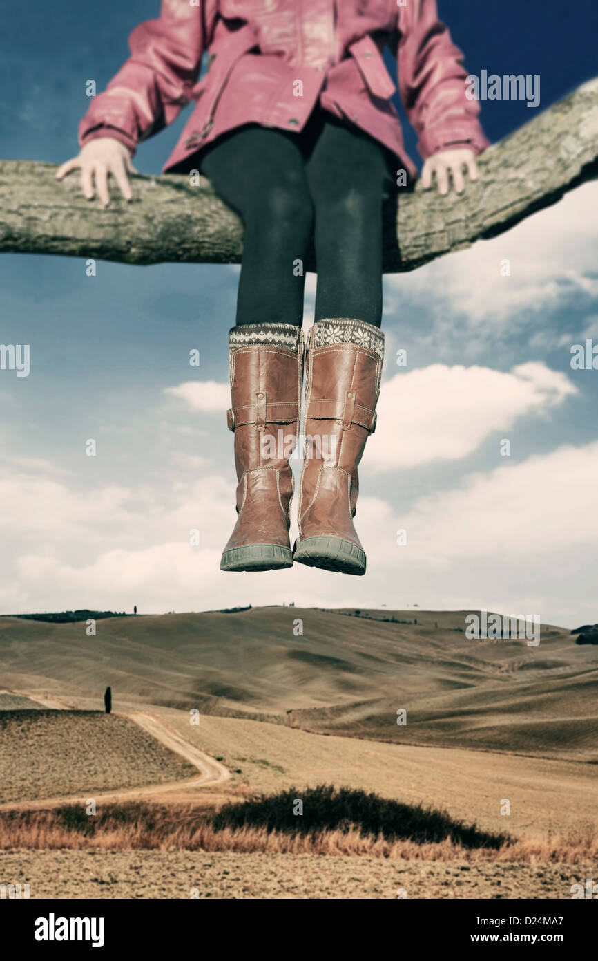 Une fille assise sur une branche au-dessus d'un champ élevé Banque D'Images