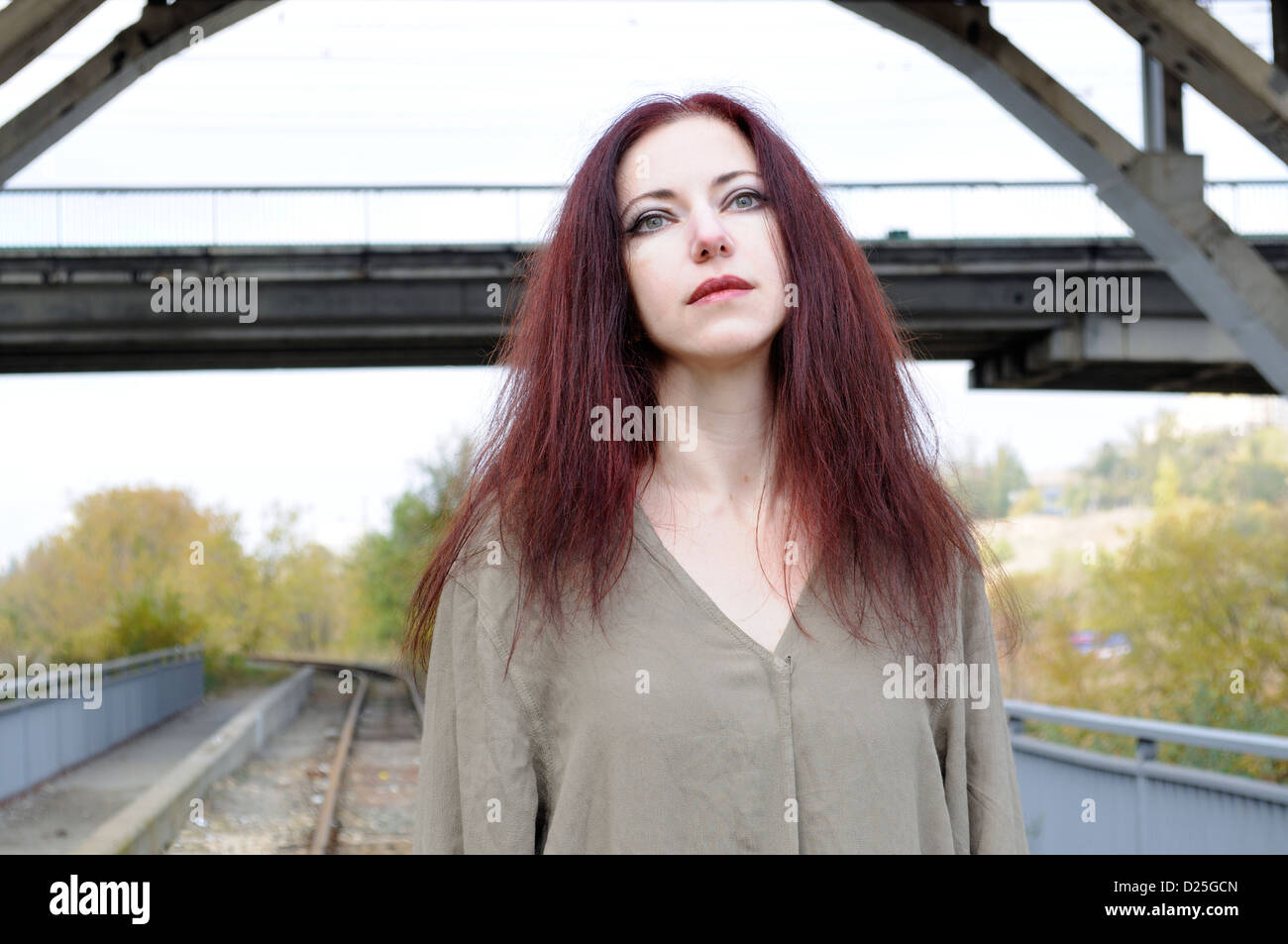 Femme triste en tunique lâche contre railroad track sous un pont Banque D'Images