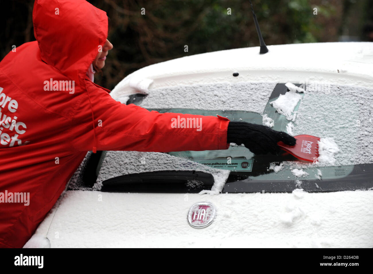 Brighton Sussex UK 14 Janvier 2013 - Jeune femme portant un Cœur rouge veste radio racler la glace et neige sur un Cinquicento Fiat Banque D'Images