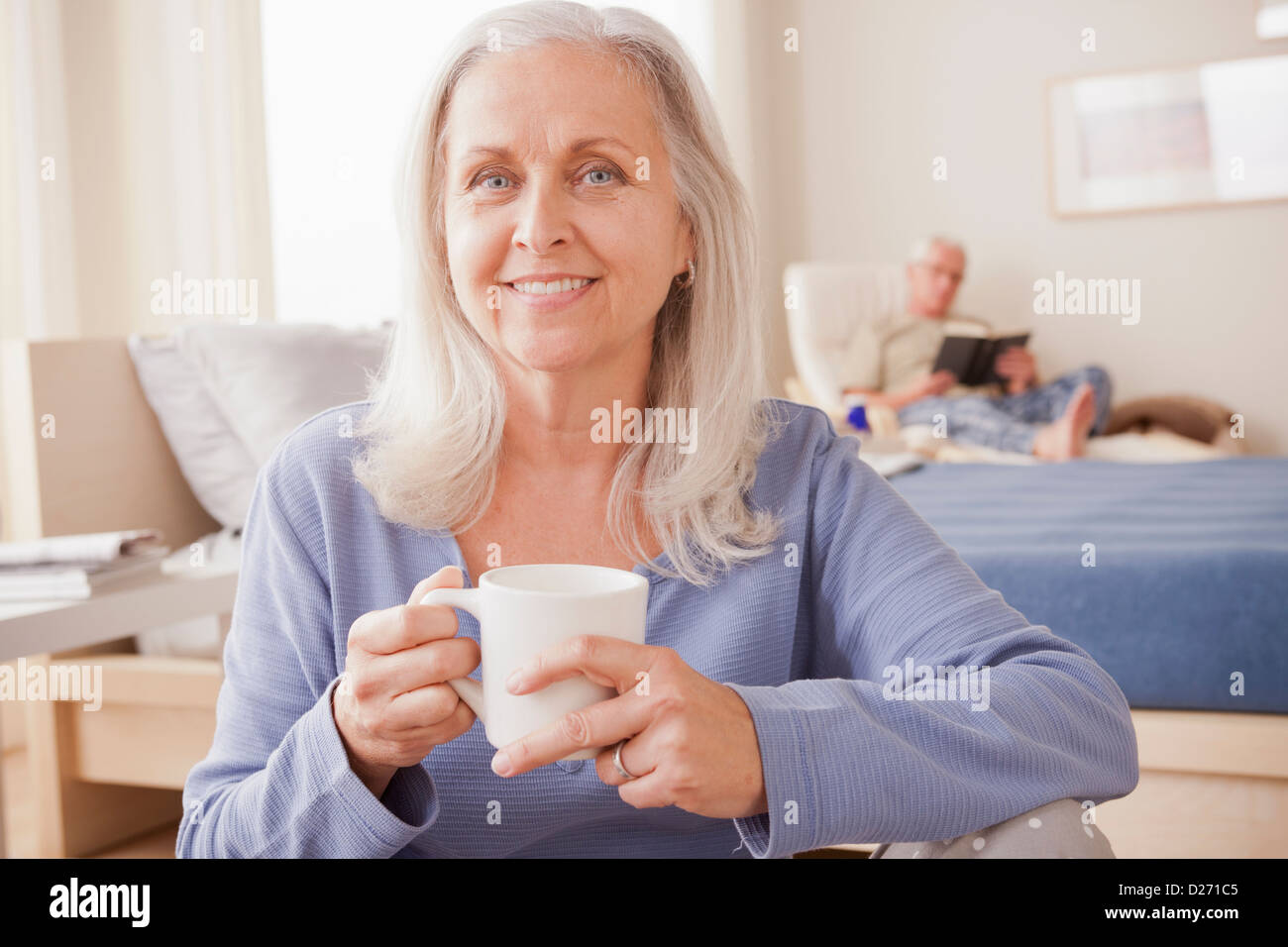 Senior woman holding Coffee cup avec mari lecture en arrière-plan Banque D'Images