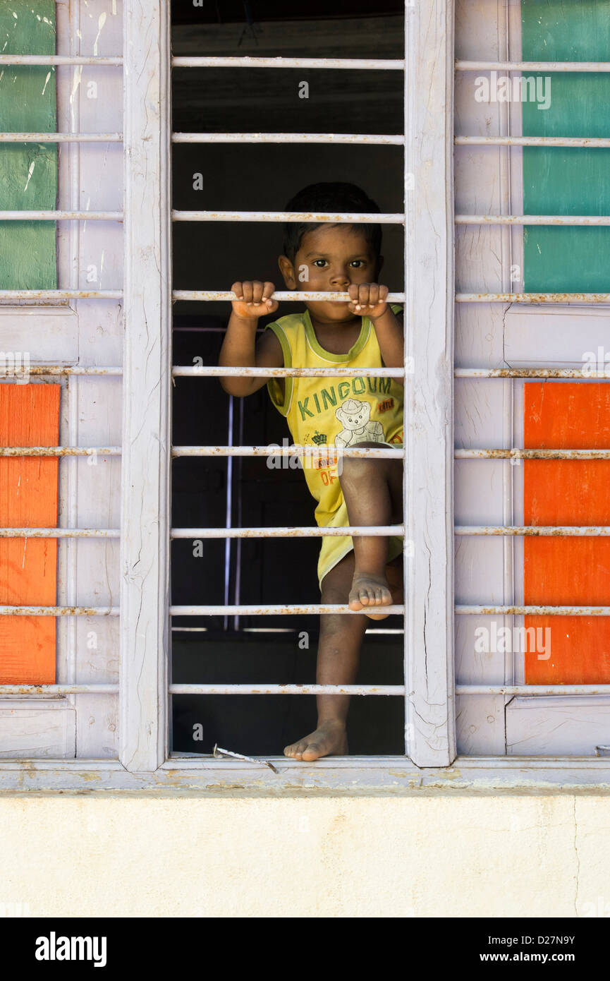 Jeune Indien village boy climbing sur fenêtre barreaux de sa maison. L'Andhra Pradesh, Inde Banque D'Images
